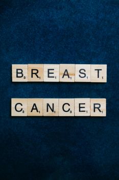 Wooden Scrabble tiles spell out 'Breast Cancer' on a dark blue background, emphasizing awareness.