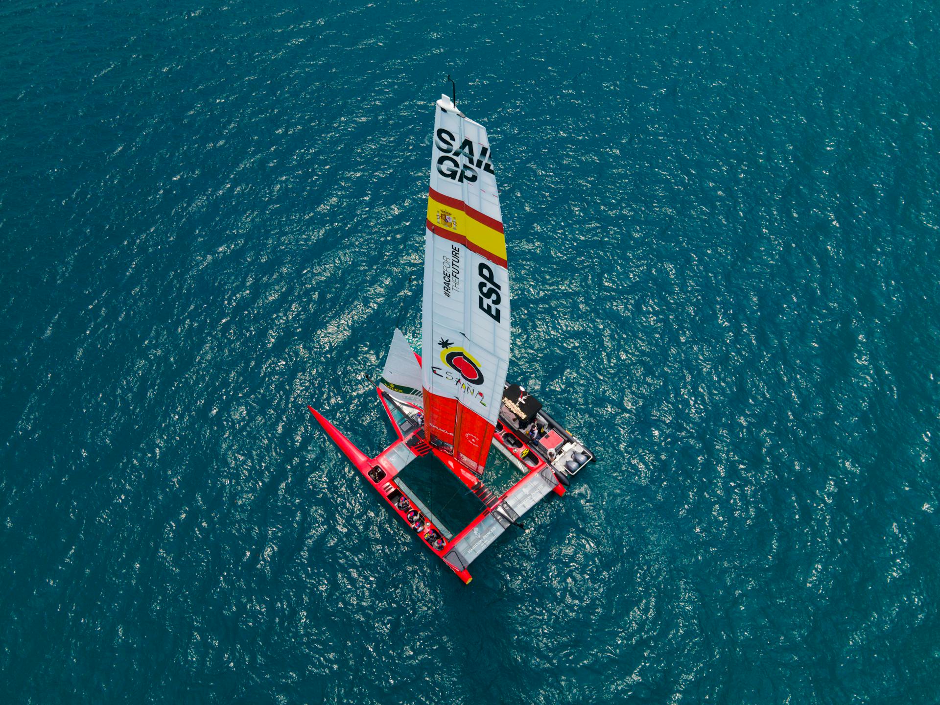 A drone shot of a vibrant red SailGP catamaran sailing in clear Bermuda waters, showcasing competitive sailing.