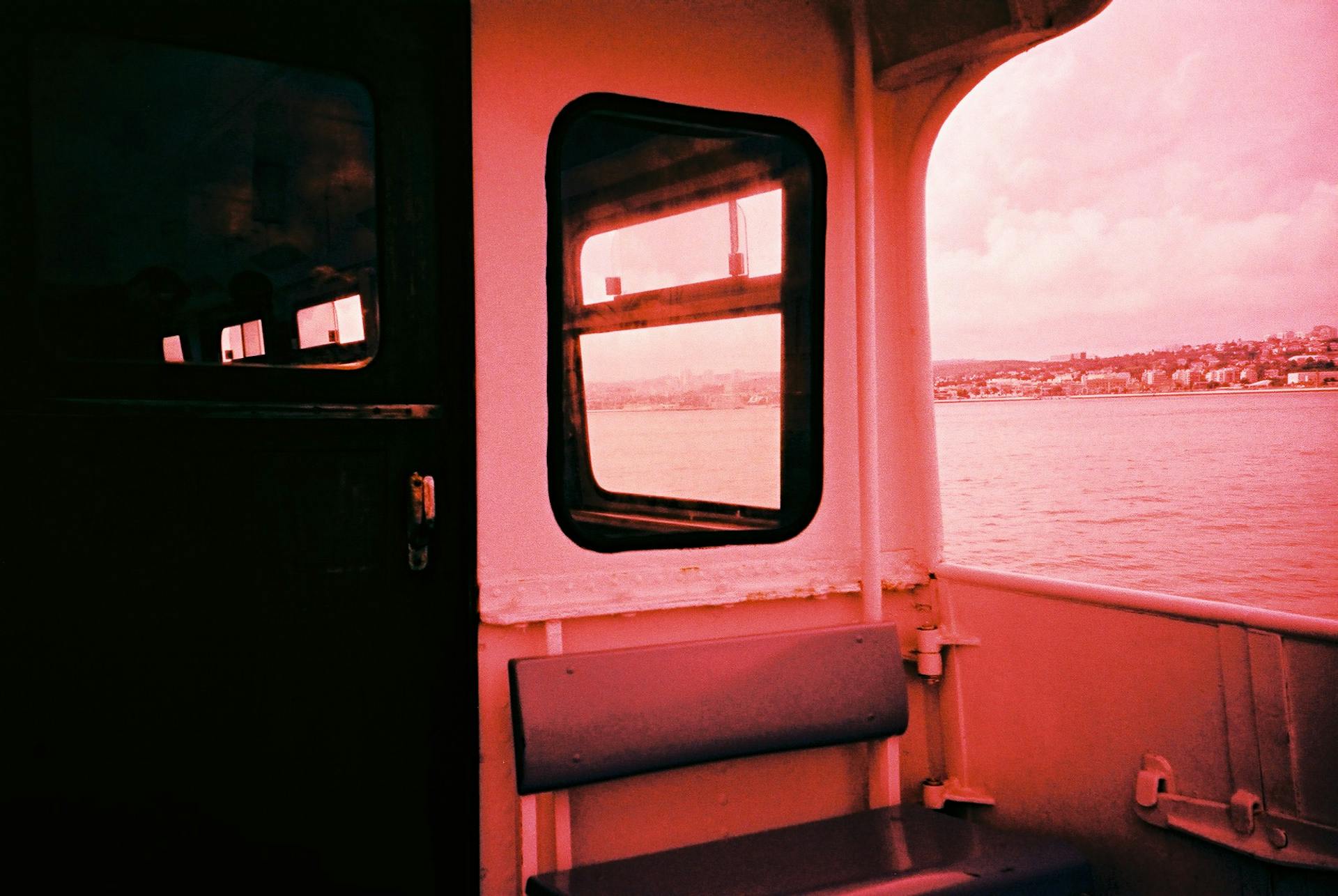 Interior view of a boat with a red hue, looking out to a coastal cityscape in Lisbon.