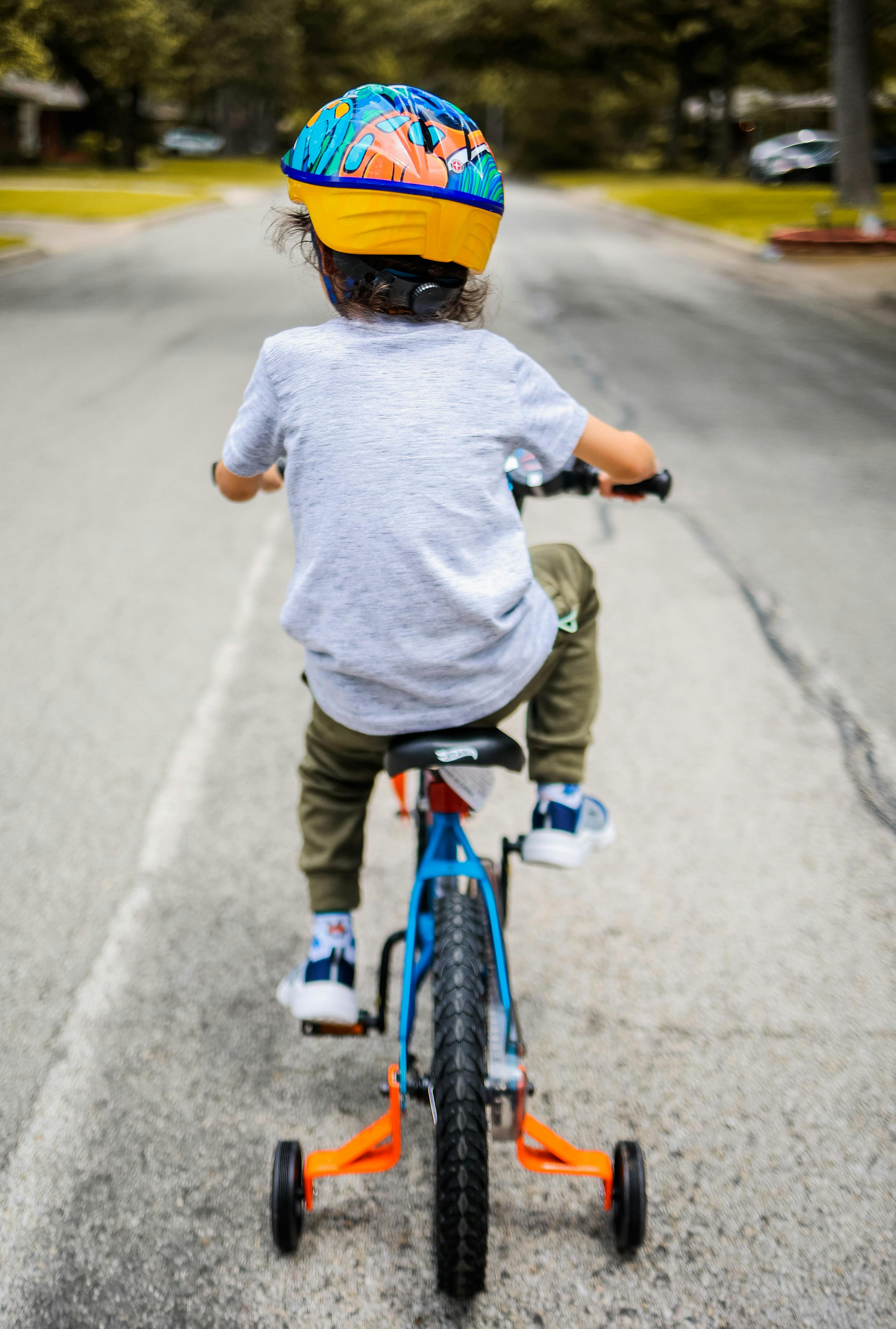 A child in a colorful helmet riding a bicycle with training wheels on an empty street.