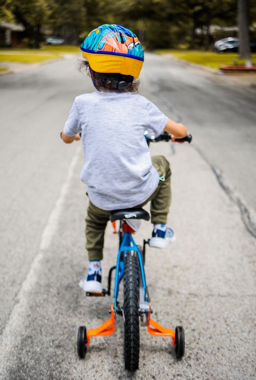 Free A child in a colorful helmet riding a bicycle with training wheels on an empty street. Stock Photo