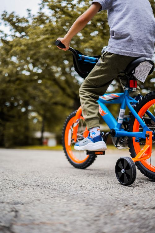 Free Child outdoors riding a colorful bicycle with training wheels on a sunny day. Stock Photo