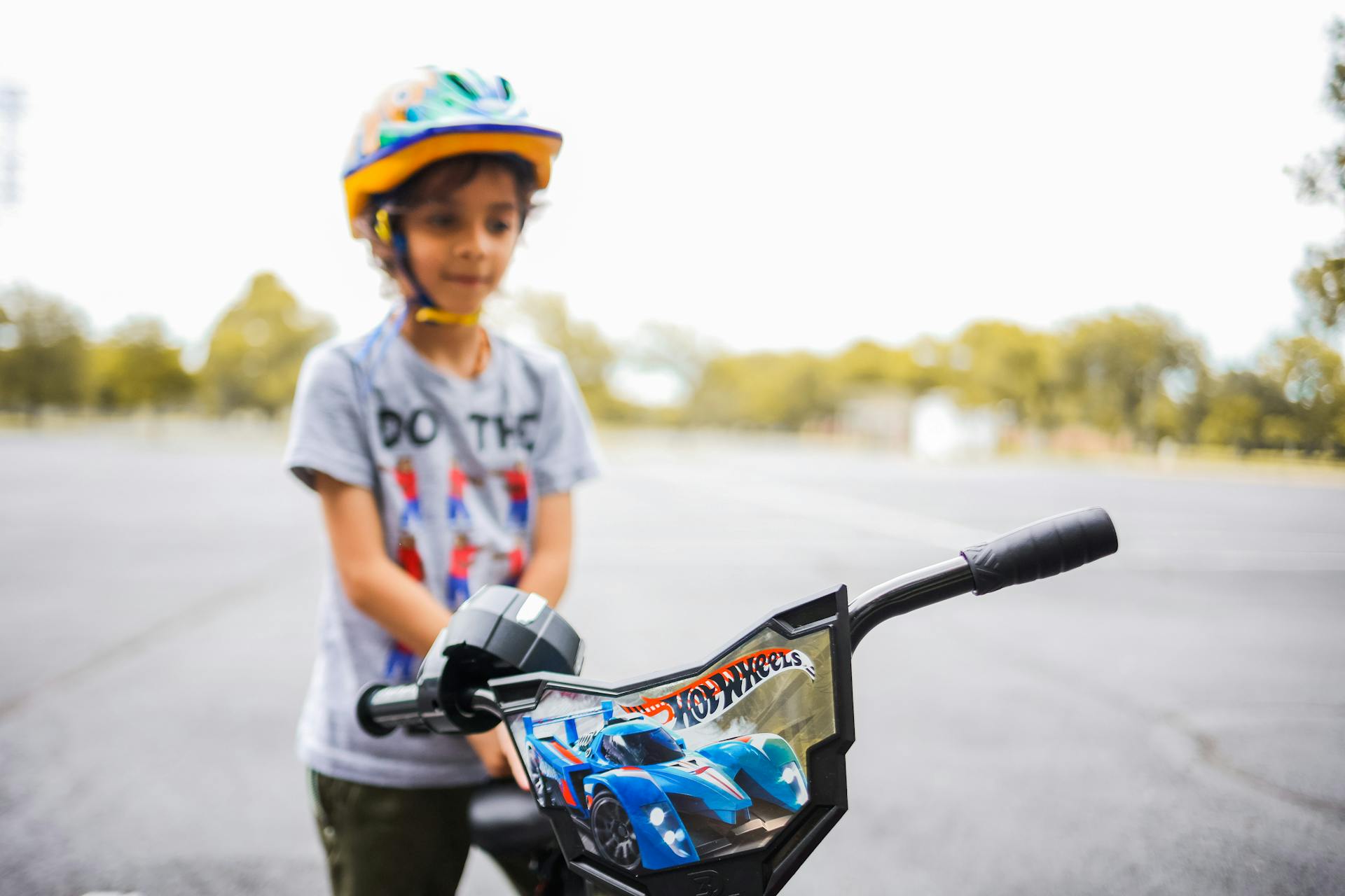 A young child wearing a helmet stands next to a bicycle in a park setting. Perfect for themes of childhood activity and safety.