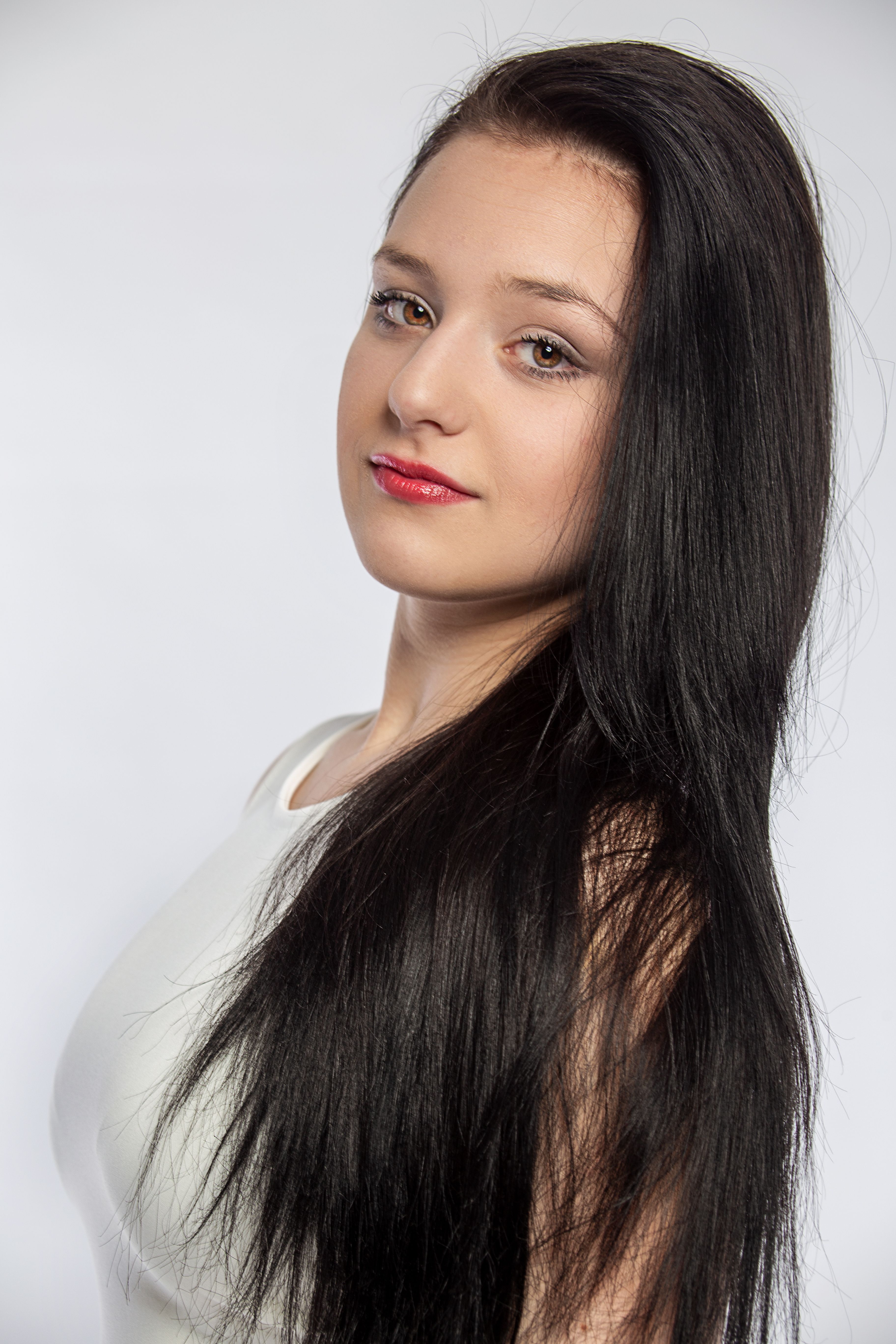 Close-up portrait of a woman with long black hair against a gray background. Studio lighting.
