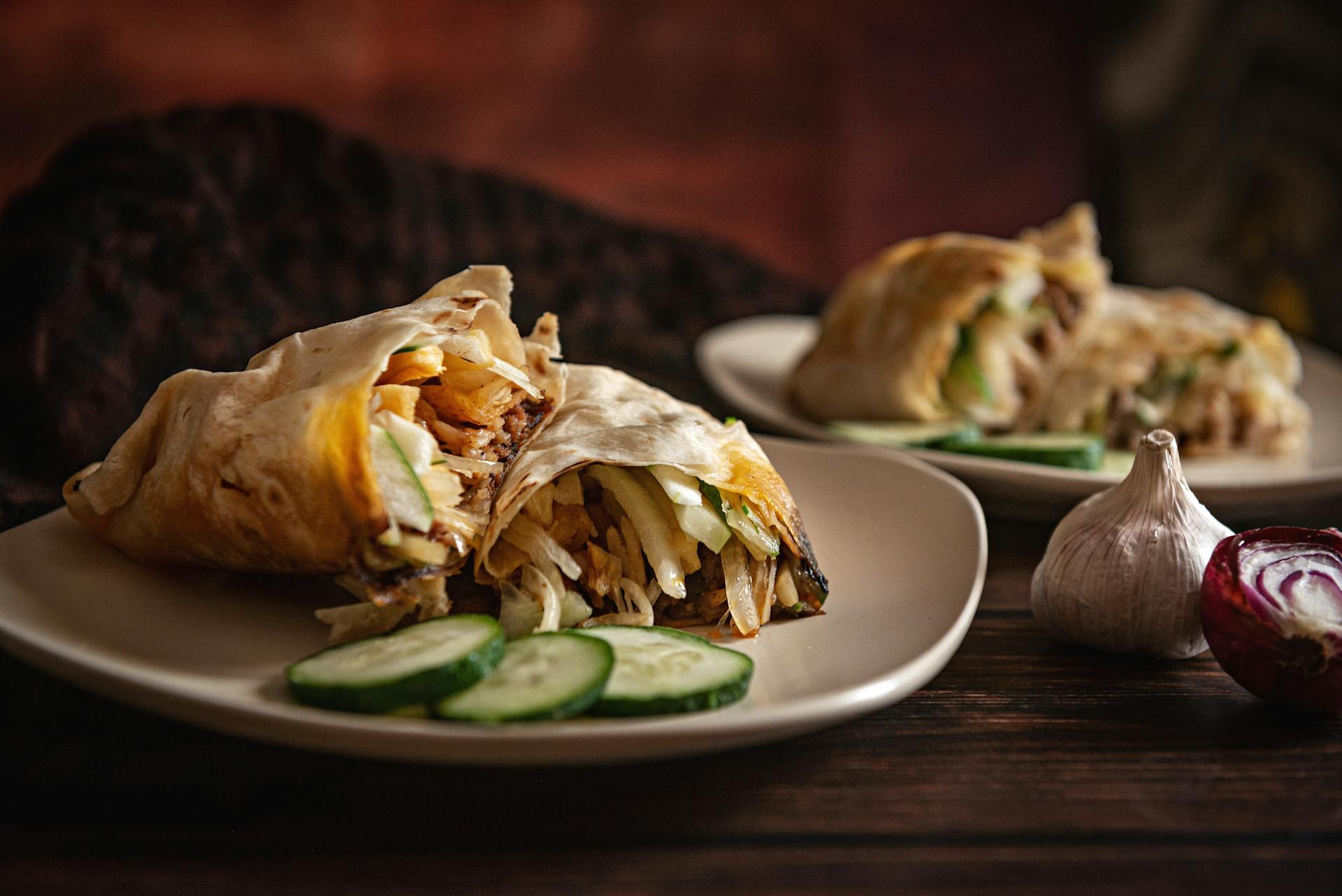 Close-up of shawarma wraps with cucumbers, garlic, and onions on plates.