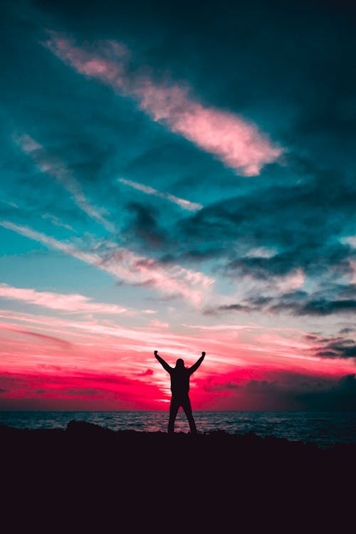 緑の雲の下で赤い夕日の光に対して手を上げる男のシルエット