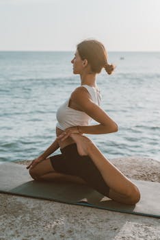 Woman performing a yoga pose by the ocean, embodying relaxation and fitness on a summer day.