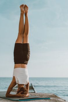 Woman performing a headstand on a dock by the ocean, promoting fitness and well-being.