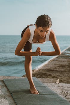Woman practicing yoga pose by the sea, embracing wellness and tranquility outdoors.