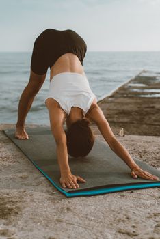 A woman performing yoga on a mat next to the sea, emphasizing flexibility and wellness.