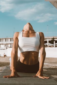 A woman in a white crop top performing yoga stretching exercises on a sunny beach.
