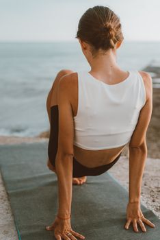 Woman practicing yoga on a mat by the ocean at sunrise.