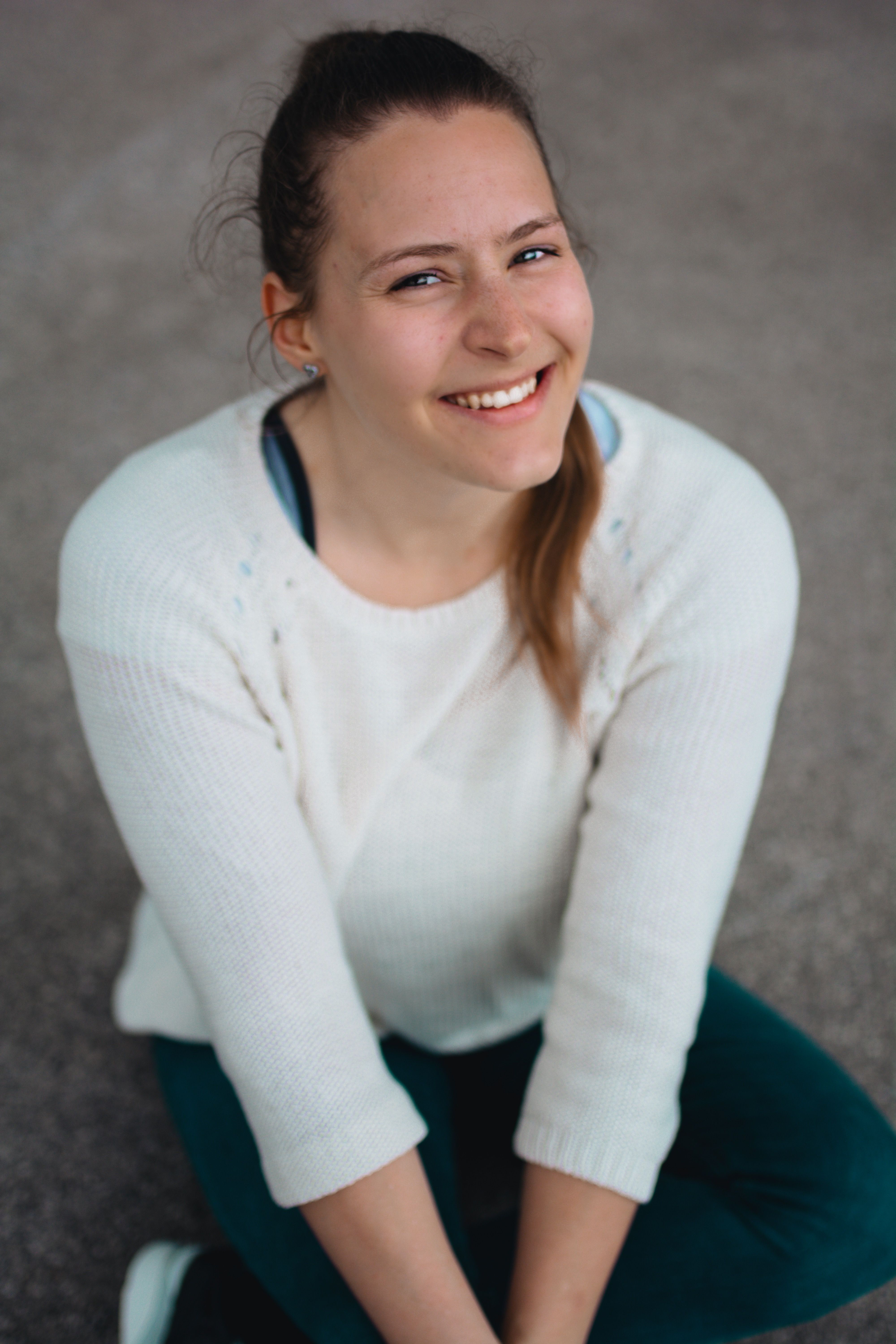 A cheerful young woman with long hair smiles warmly while sitting outdoors.