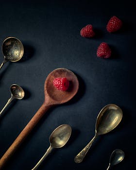Artistic flat lay of vintage spoons and fresh raspberries on dark background.