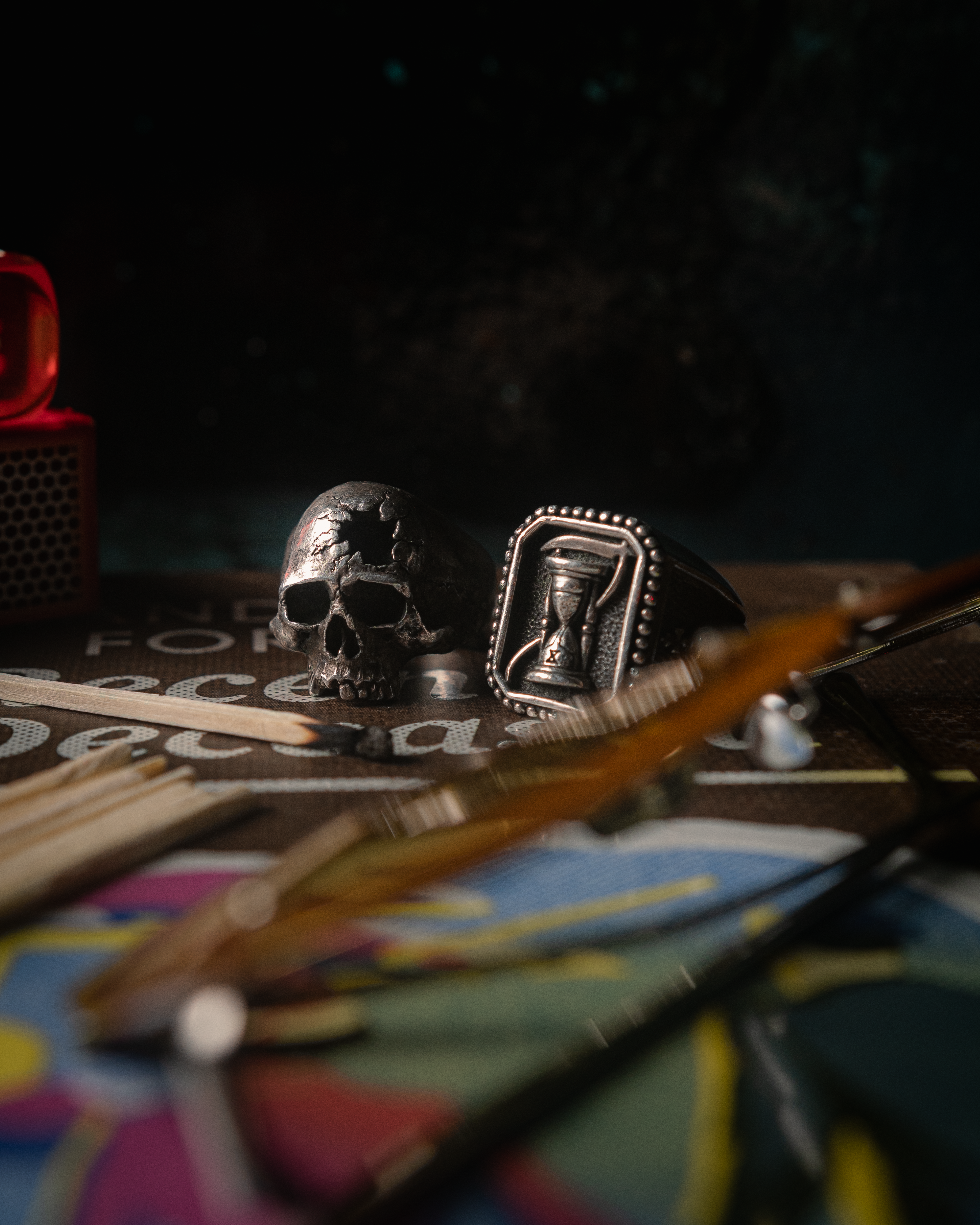 Dark themed close-up of a skull and hourglass rings on a textured surface, adding a vintage feel.