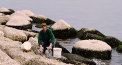 一名戴着彩色无檐帽的男子在岩石海岸附近抱着一只章鱼