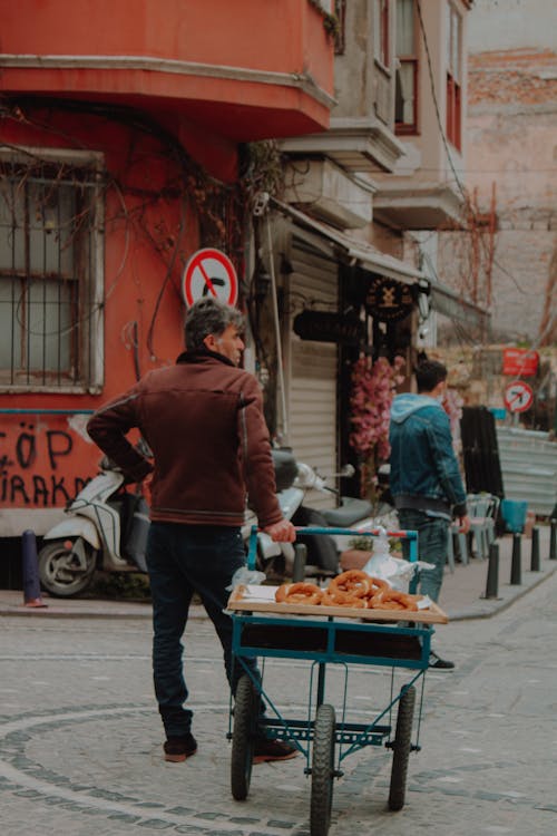 A Man in Brown Jacket Standing Beside a Food Cart