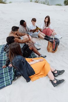 Friends enjoying a beach day, seated on the sand with a picnic setup.