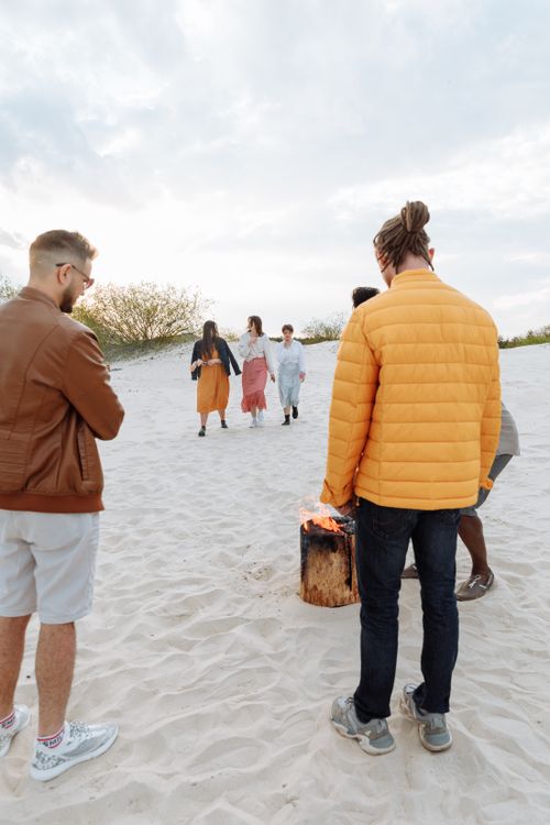 Free Group of friends enjoying a sunset beach gathering around a campfire in sand dunes. Stock Photo
