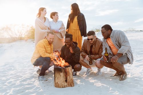 Free A diverse group of friends enjoying a bonfire on a sandy beach during the day. Stock Photo