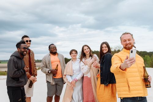 Free A diverse group of friends smiling and taking a selfie outdoors with drinks, capturing joyful moments together. Stock Photo