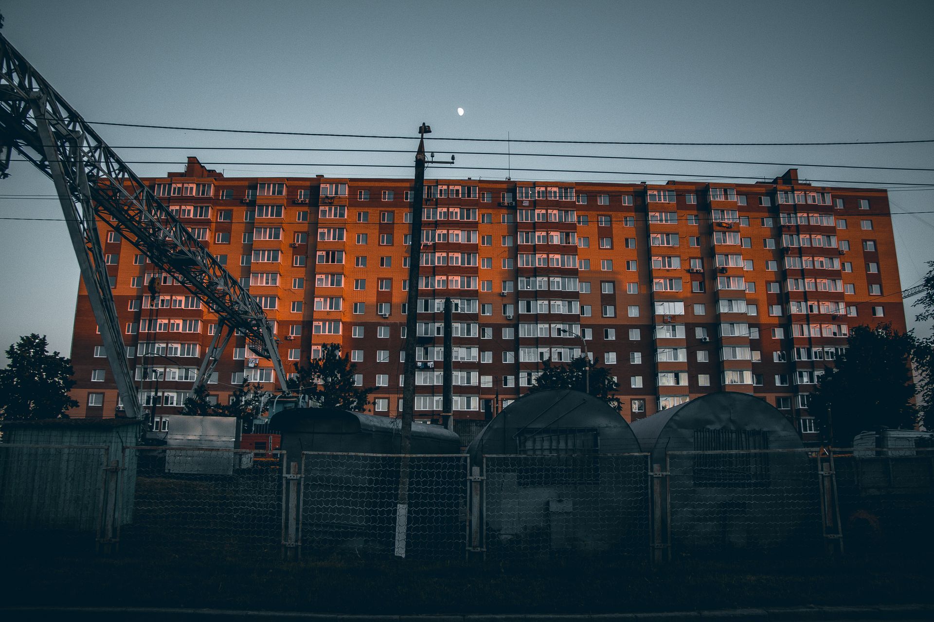 Dramatic view of a modern apartment complex at twilight with industrial elements in foreground.