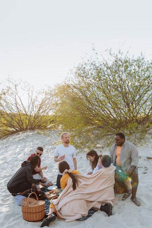 Free A diverse group of friends bonding over a picnic on the beach during a sunny day. Stock Photo
