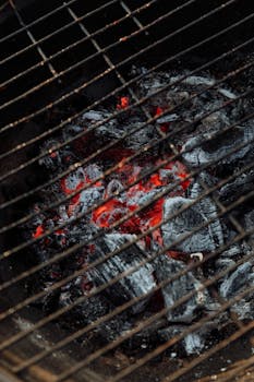 Detailed view of a charcoal grill with glowing red embers and ash, perfect for barbecue enthusiasts.