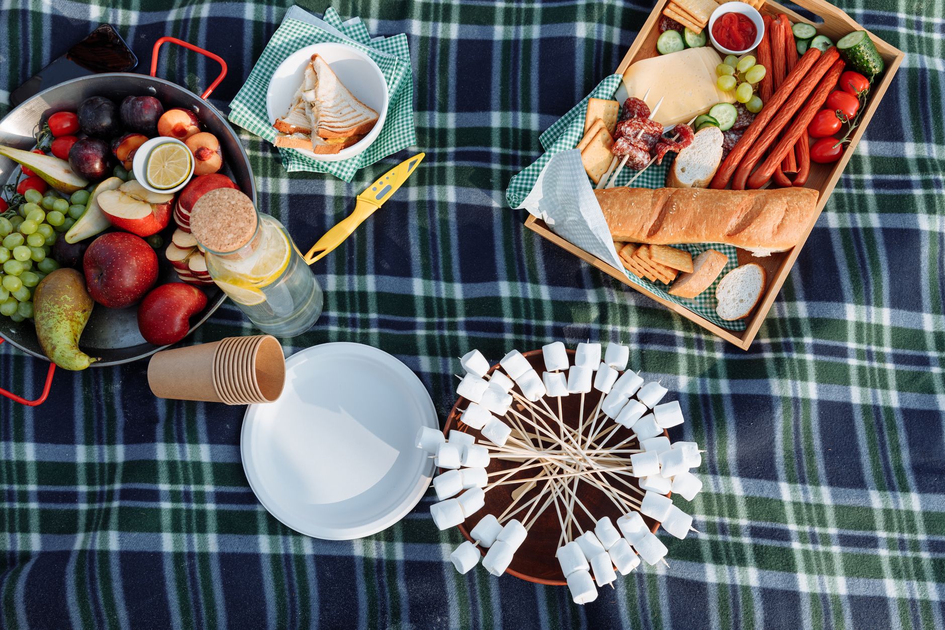 A vibrant picnic featuring fresh fruits, sandwiches, and marshmallows on a blanket.