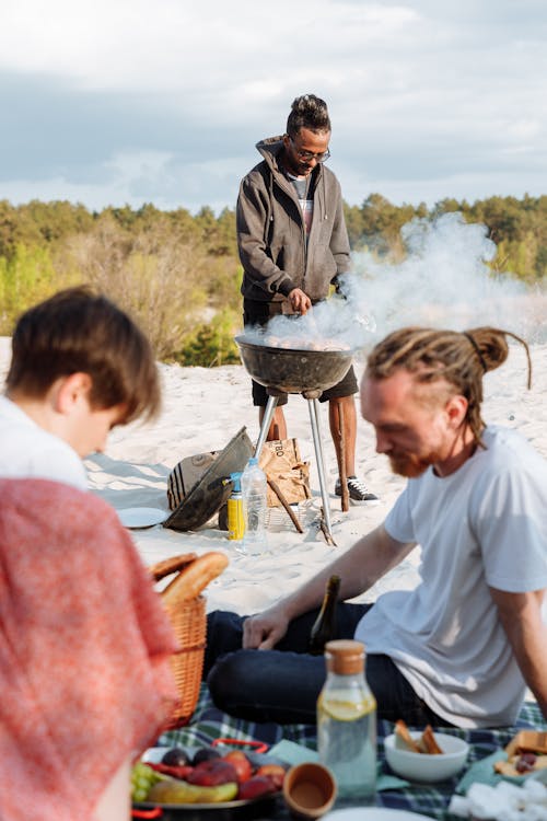 Free A Man Grilling Near Two People Sitting on a Picnic Blanket Stock Photo