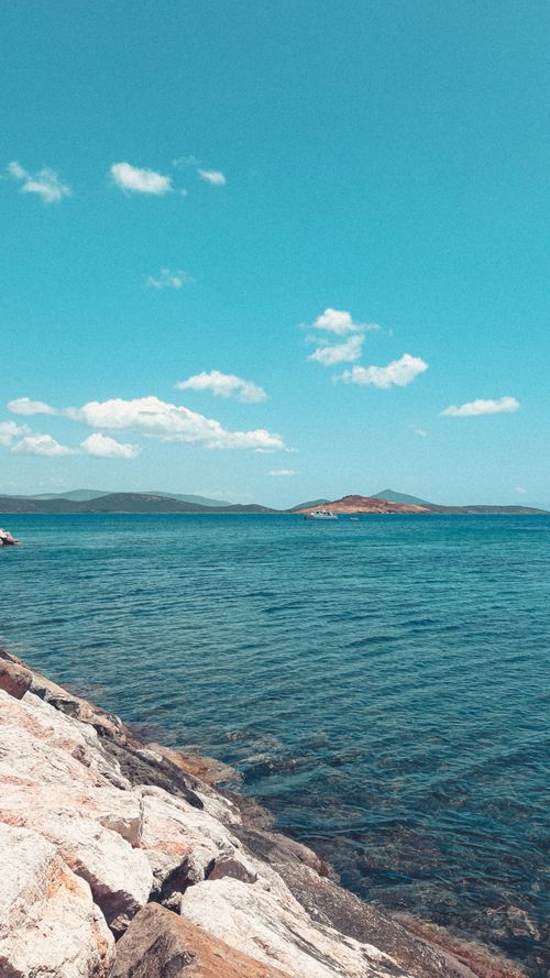 Free A tranquil seascape with clear blue skies and a rocky shoreline, perfect for relaxation themes. Stock Photo