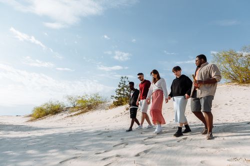 Free Diverse group of friends enjoying a walk on a beautiful sandy beach under a clear sky. Stock Photo
