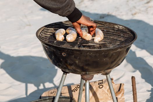 Hand placing sausages on a charcoal grill outdoors, setting a perfect summer cookout scene.
