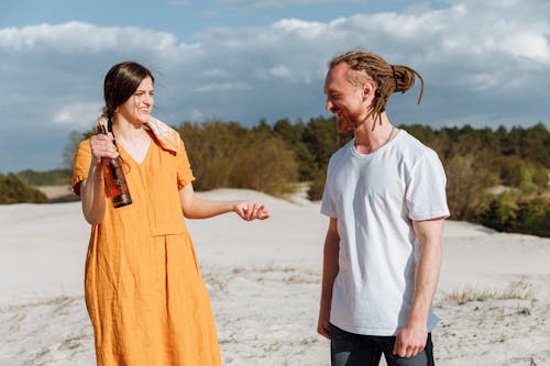 Woman in Orange Dress with Beer Bottle Talking to a Man in White Crew Neck Shirt
