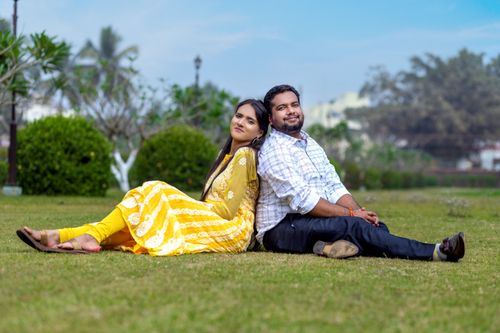 Free A joyful couple sitting back-to-back on green grass in a sunny park. Stock Photo