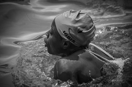 Grayscale Photo of a Person Swimming with Swim Cap