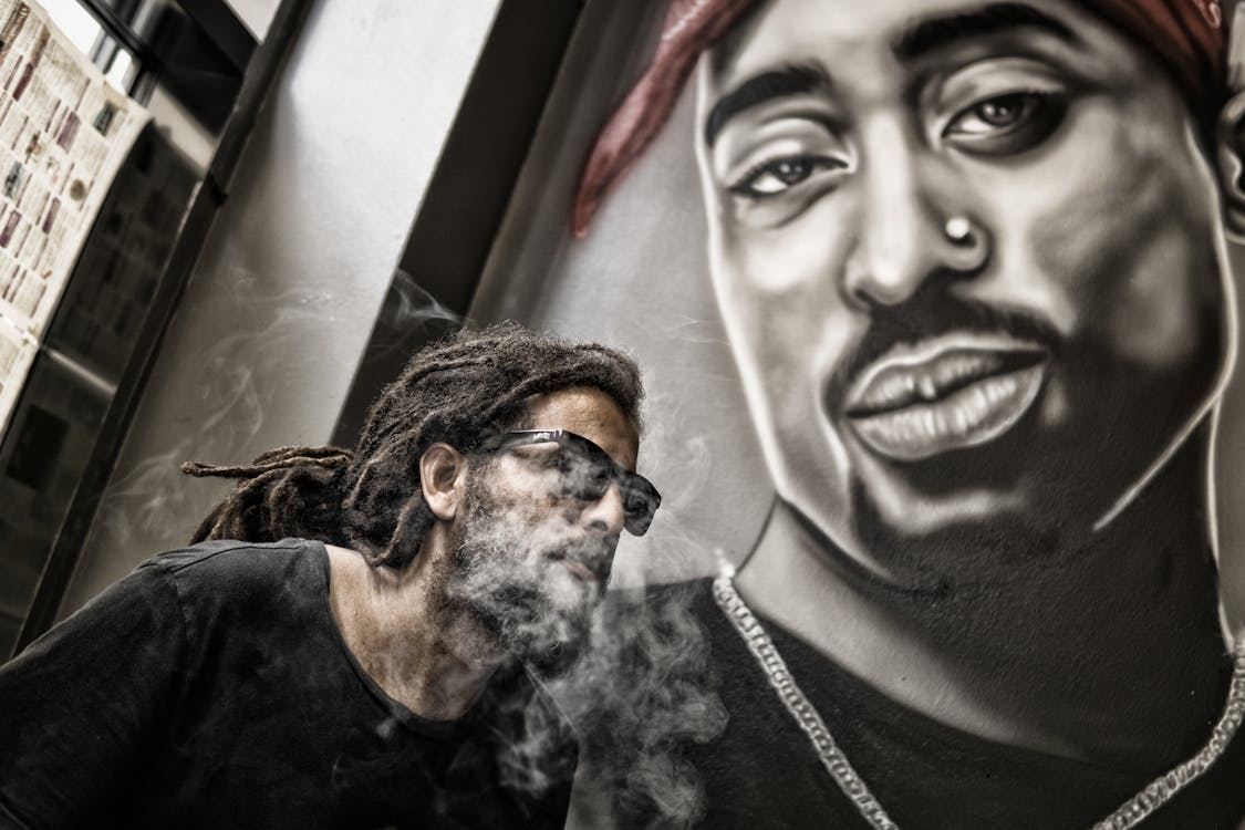 Free Man With Dreadlocks and Sunglasses Poses Near Tupac Shakur Portrait Stock Photo