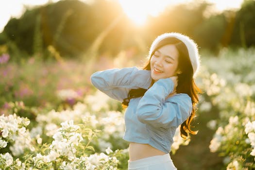 A cheerful woman in a blue crop top enjoying a flower garden during sunrise in Laos.