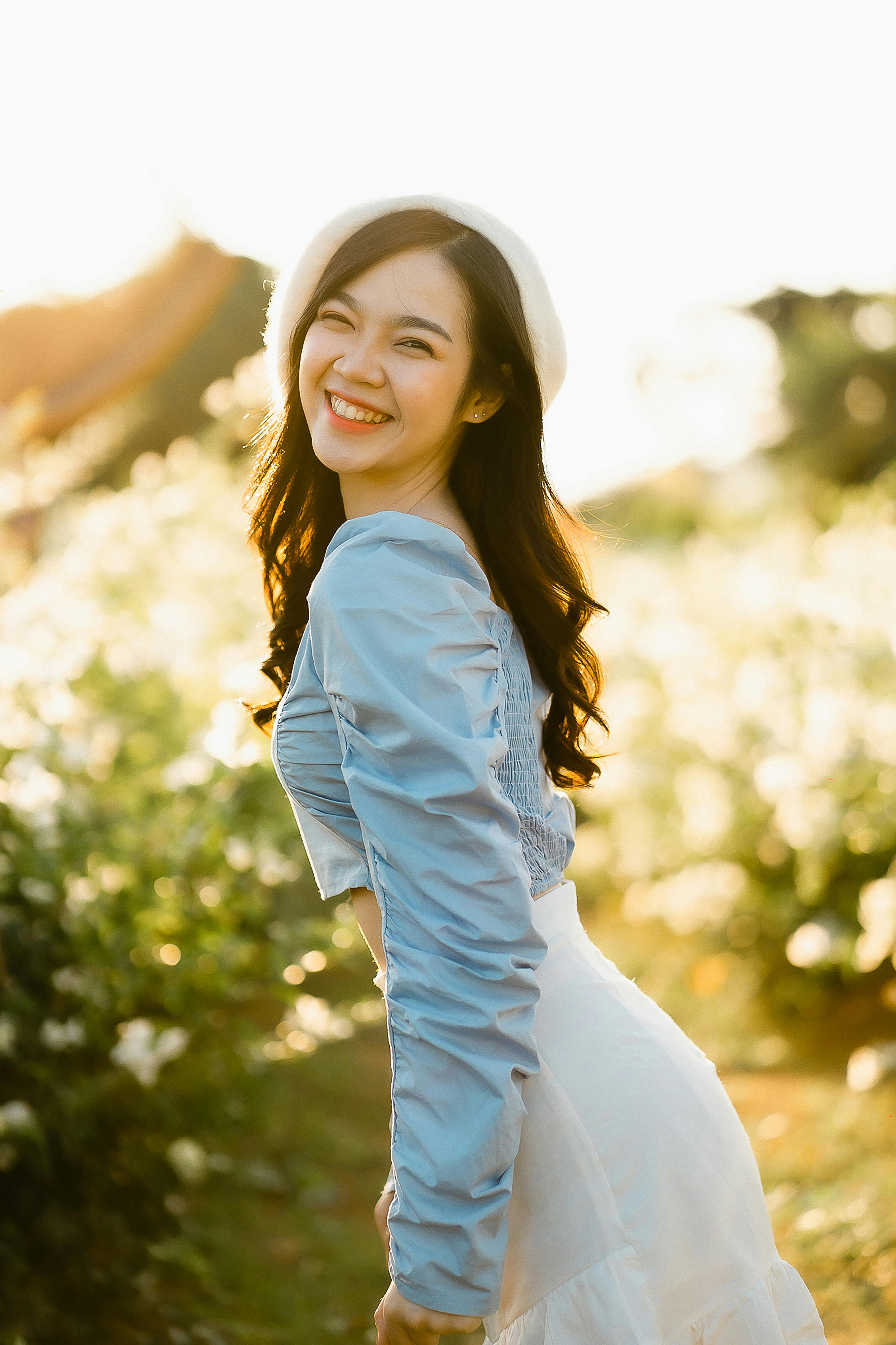 Cheerful woman in a blue top and white skirt smiling brightly in a sunlit garden.