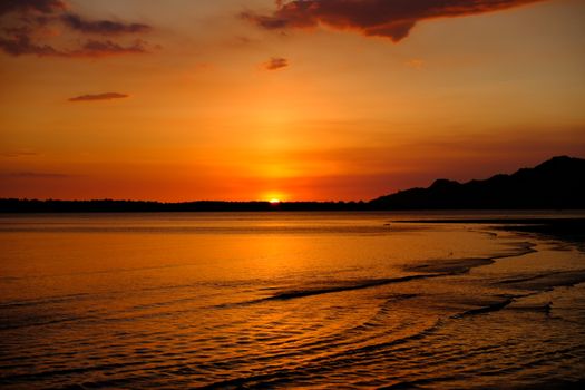 Beautiful sunset over a calm ocean with dramatic clouds and golden hues reflecting on water.