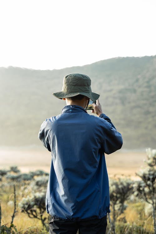 Man in Blue Jacket Taking Pictures of Field by Phone 