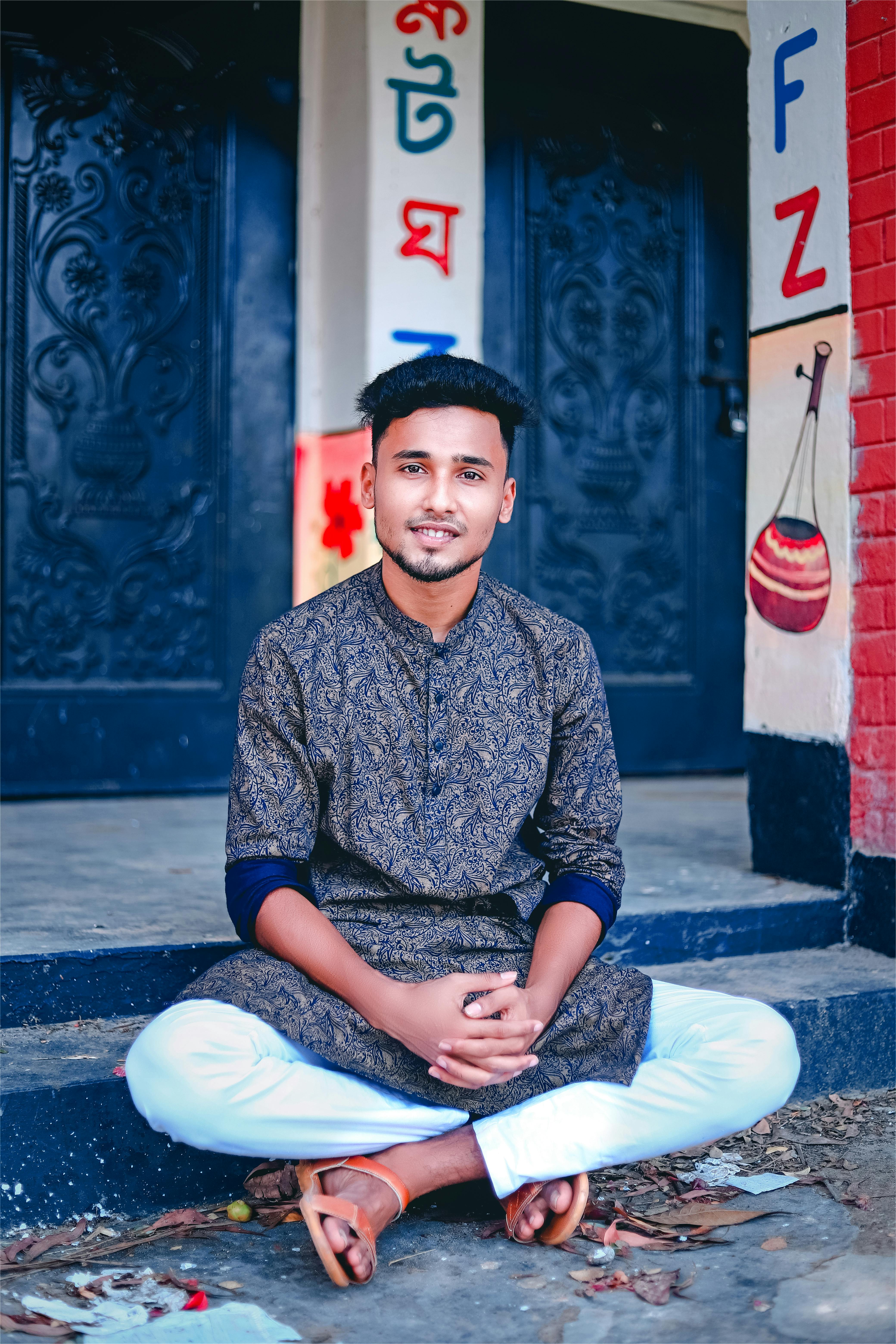Confident young man in traditional outfit sitting outdoors with colorful backdrop.