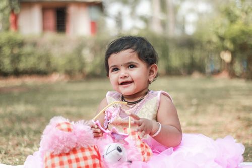 Free Cute toddler girl smiling while playing with soft toys outdoors in an Indian garden. Stock Photo