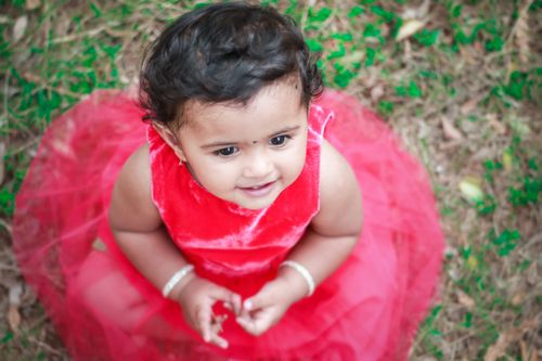 Free A joyful toddler in a red dress smiling on a grassy outdoor setting. Stock Photo