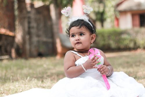 Free Adorable Indian toddler girl in white dress holding toy outdoors. Stock Photo