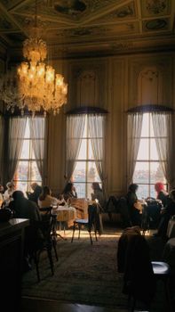 Elegant restaurant interior with a chandelier and scenic window view, featuring diners.