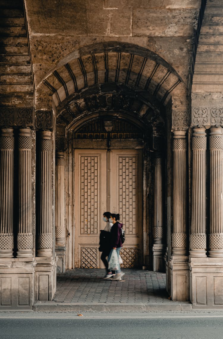 People Wearing Face Mask Walking Near An Ancient Building 