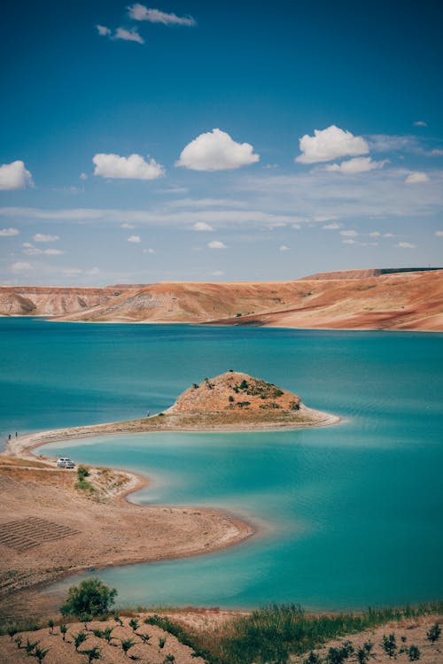 Picturesque landscape of peaceful lake located near sandy hills with dry green grass under cloudy blue sky