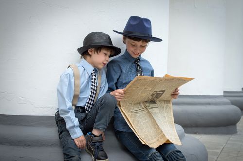 Free Two young boys in hats share a moment reading a newspaper, showcasing vintage style and curiosity. Stock Photo
