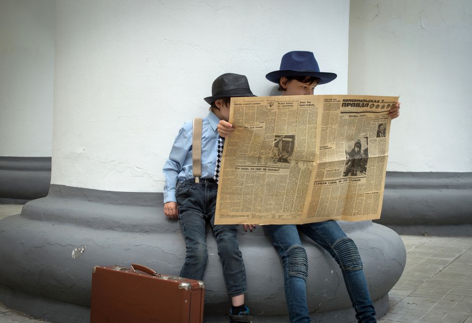 Dos niños estilosos con gorras leyendo un periódico vintage al aire libre.